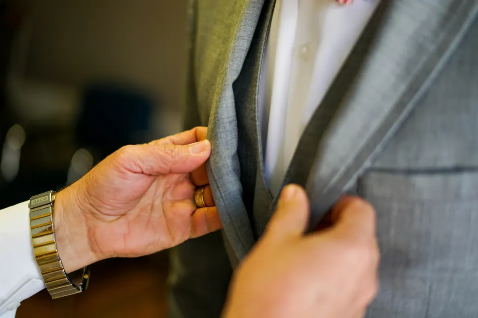 Hands checking the lapel and front edge of a grey suit jacket