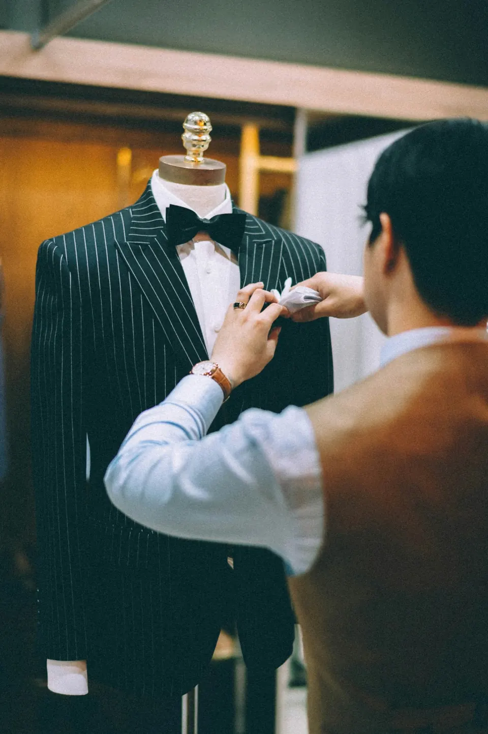 Tailor inspecting a pinstripe dinner jacket on a dress form, seen from behind