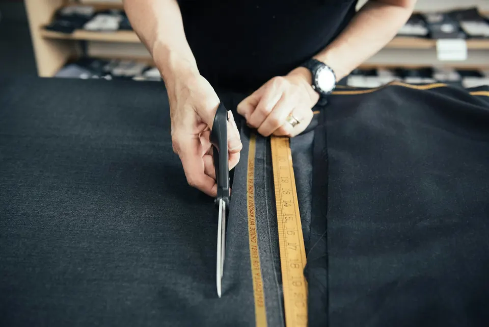 Hands cutting dark suiting wool with shears along a wooden yardstick